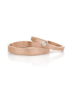 Handgemaakte roségouden trouwrigen met een diamant in de damesring, mat oppervlak en gepolijste randen.