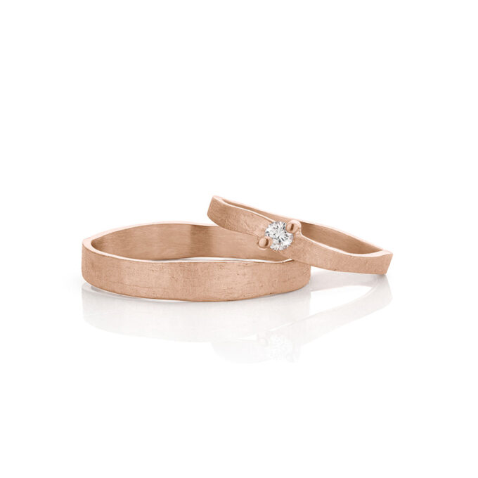Sierlijke roségouden trouwrigen met een diamant in de damesring, mat oppervlak en gepolijste randen.