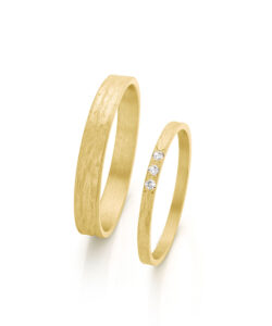 Pair of handmade yellow gold wedding rings with embossed finish and three subtle diamonds in ladies ring.