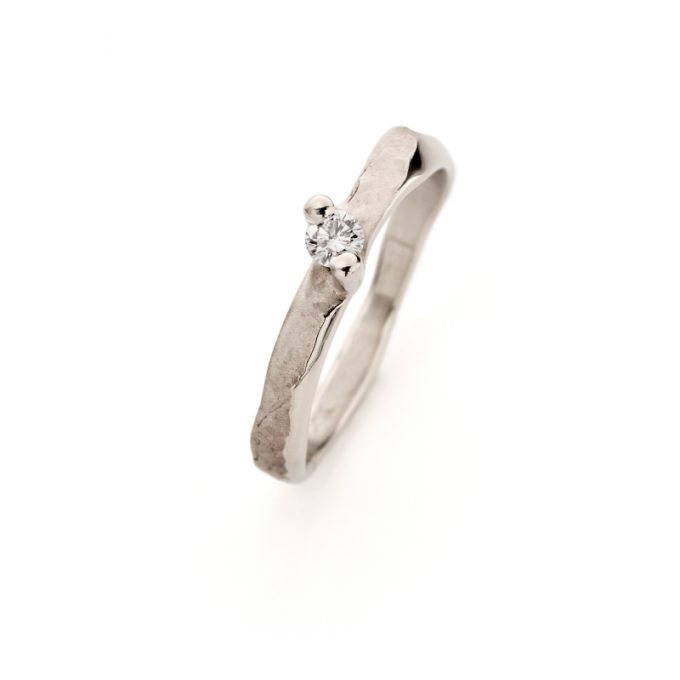 Playful engagement ring in white gold with matte finish and uneven polished edges, featuring a brilliant diamond at the center.