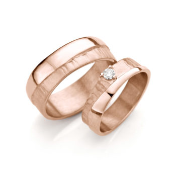 Elegante handgemaakte roségouden trouwringen met glad gepolijst oppervlak, een onregelmatige matte afwerking en een diamant op de damesring.