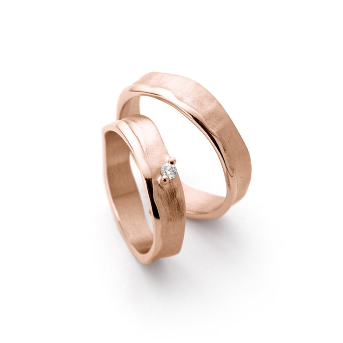 Handmade wedding rings with matte irregular finish, wide polished edges and one diamond in the ladies ring.