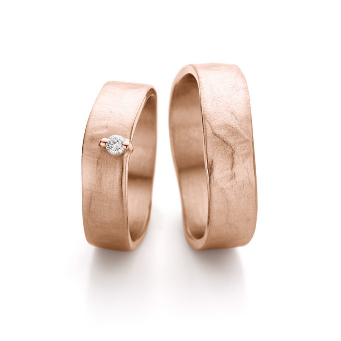Brede elegante roségouden trouwringen met matte afwerking, gepolijste rand en sierlijke diamant in damesring.