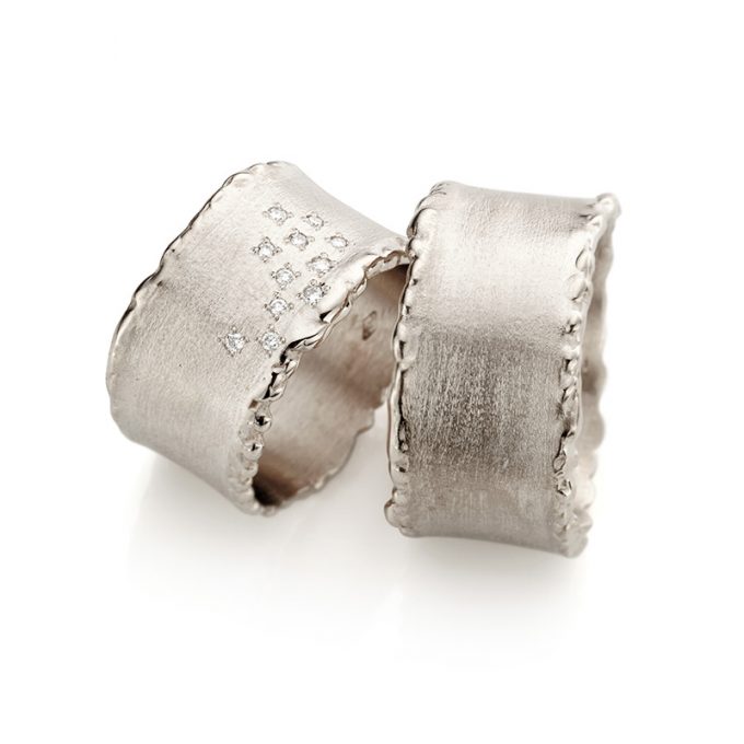 Sparkling matte white gold wedding rings with eleven diamonds in the women's ring and polished scrolled edges.