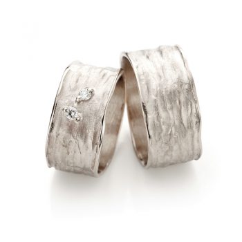 Shimmering white wedding rings with polished edge, rough finish and two diamonds in ladies ring.
